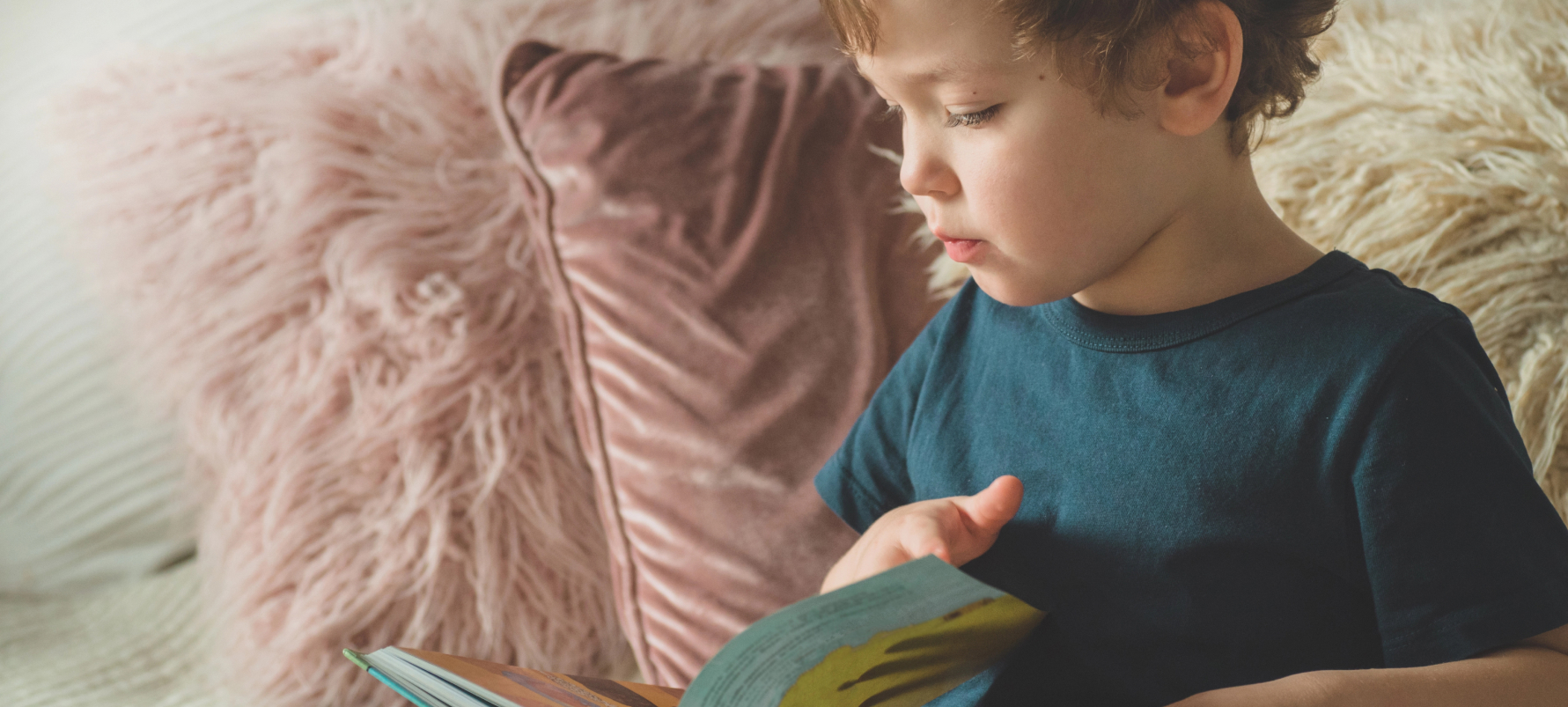 Kleine jongen op een bank met kussens een boek te lezen