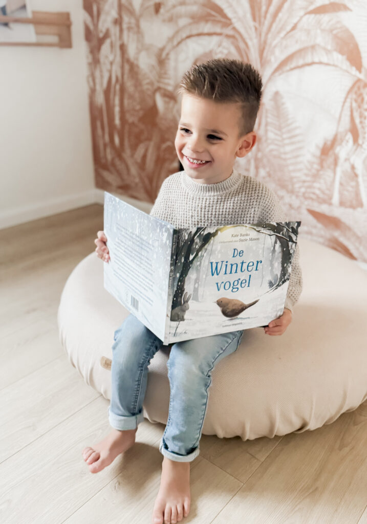 Kleine jongen zit op een poef een boek te lezen