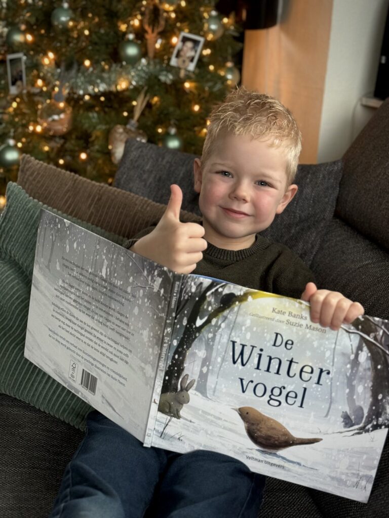 Kleine jongen zit op een bank met een boek in zijn hand en een duim omhoog