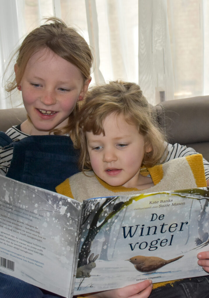 Twee zussen zitten op een bank een boek te lezen