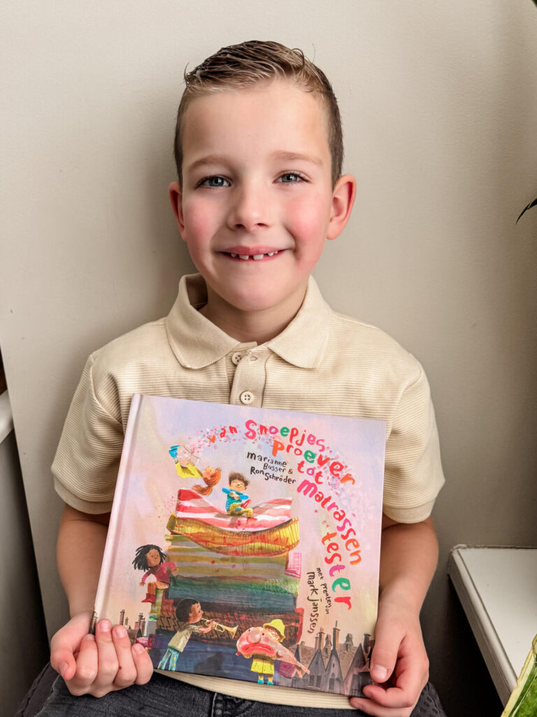 Blije jongen houdt trots het boek Van Snoepjesproever tot Matrassentester vast en lacht naar de camera.