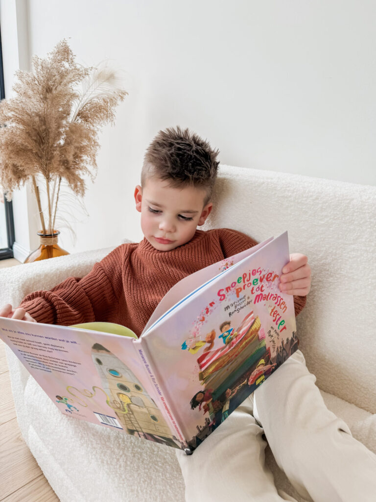Jonge jongen zit ontspannen in een stoel en leest geconcentreerd het boek Van Snoepjesproever tot Matrassentester.