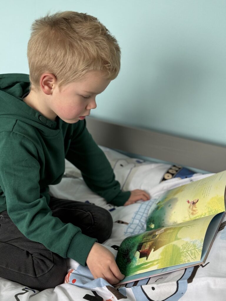 Jonge jongen zit op zijn bed en bladert aandachtig door een kleurrijk prentenboek.