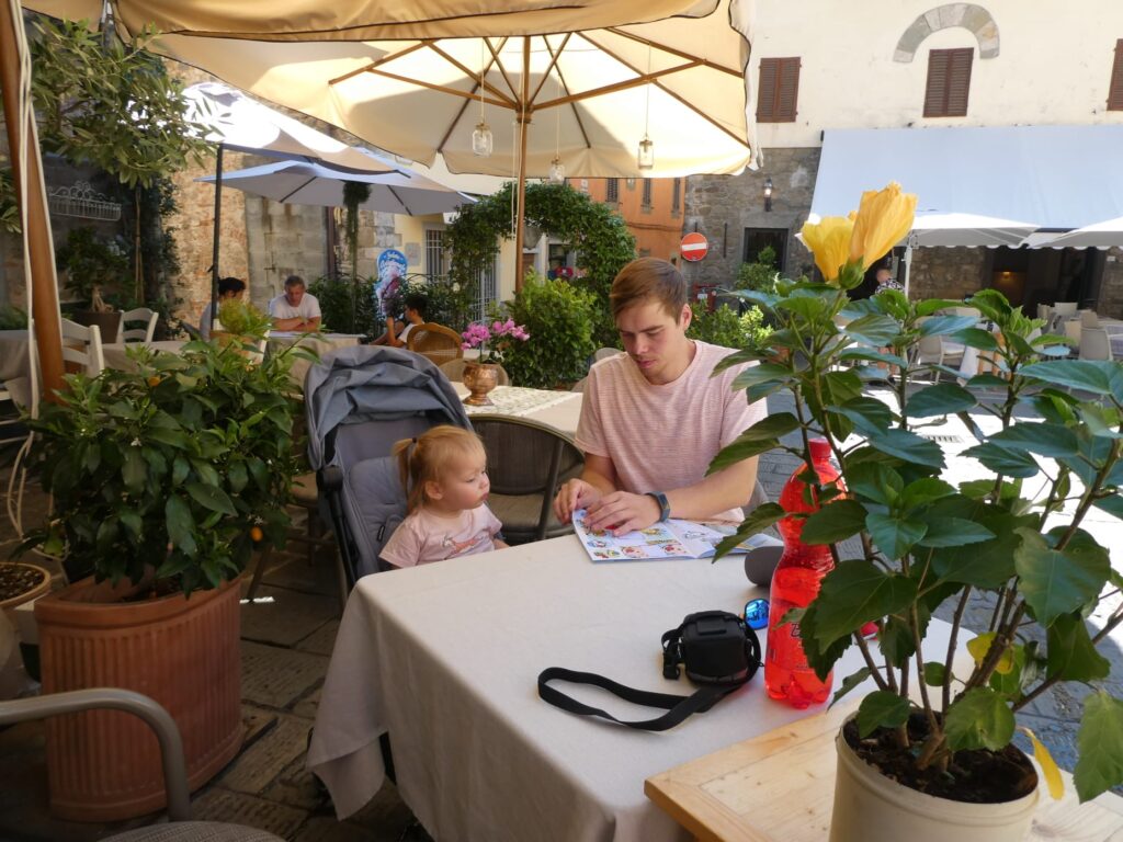 Vader en dochter lezen samen een kinderboekje op een zonnig terras tijdens de vakantie.