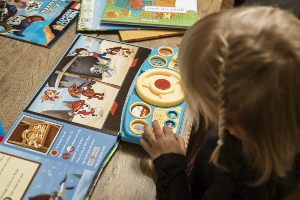 Klein meisje speelt met een interactief Paw Patrol boek vol knoppen en leest samen spannende avonturen tijdens vakantie.