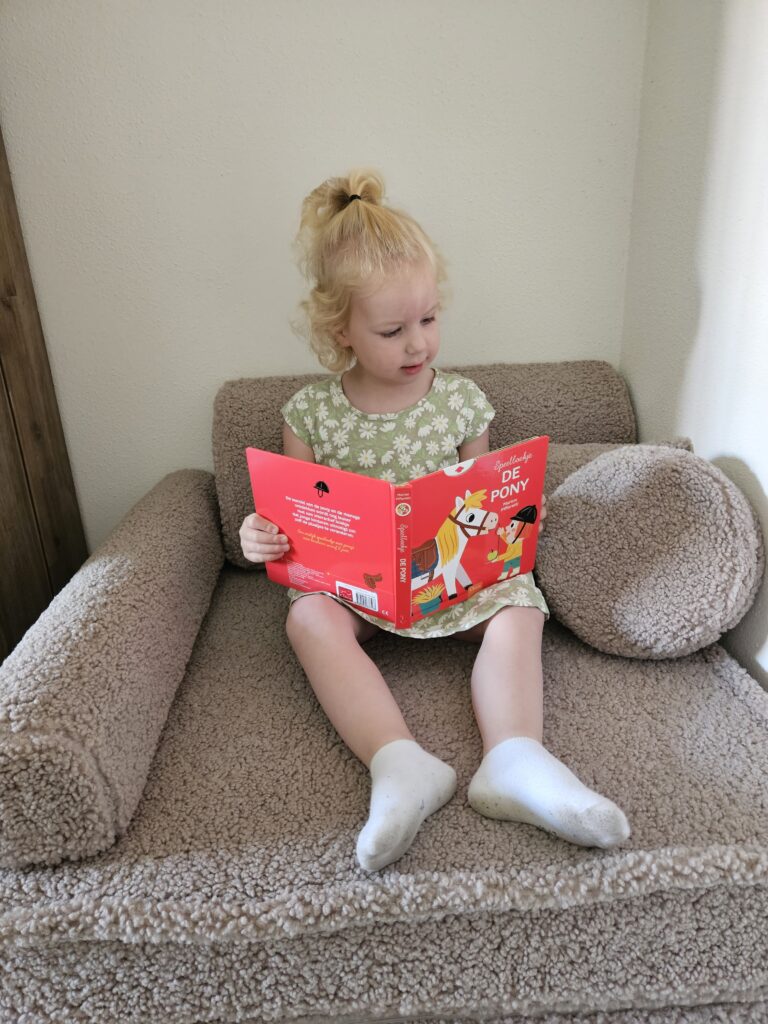 Klein meisje uit het Kinderboekjes.nl kinderpanel zit op een stoel en leest lachend in het interactieve boekje De Pony.