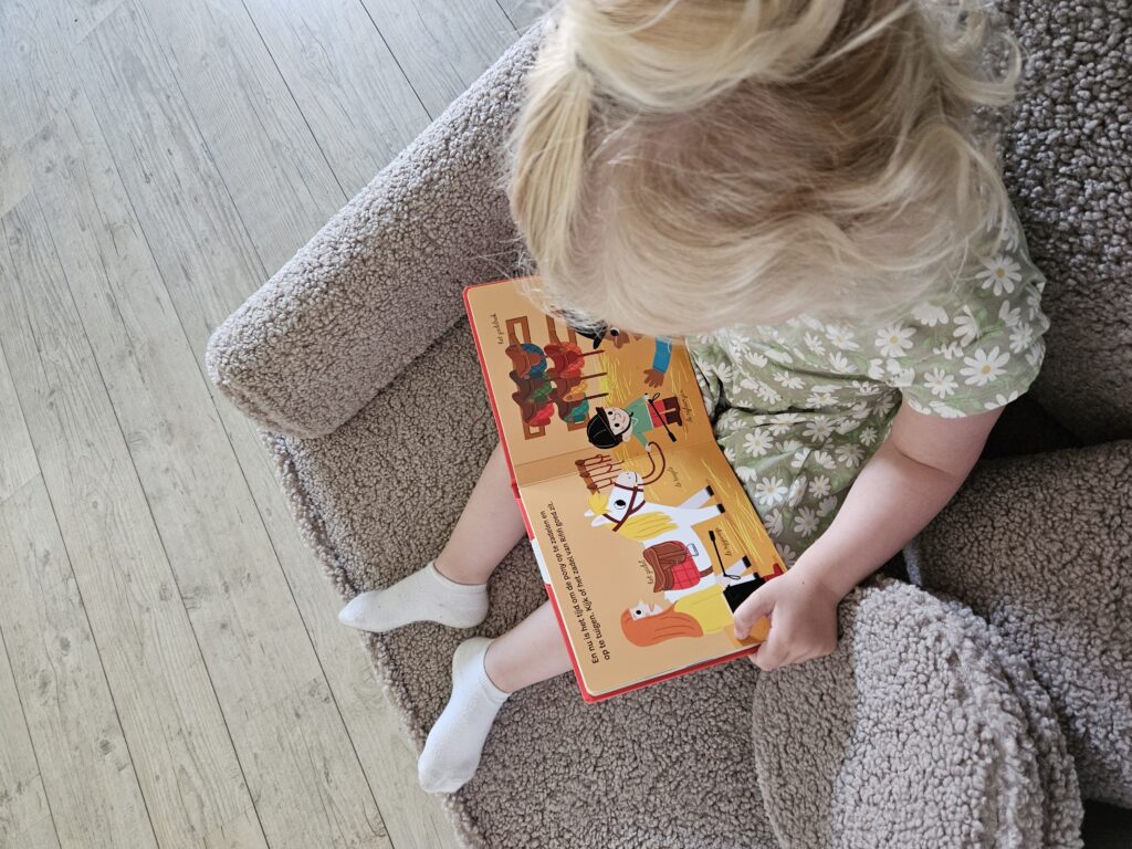 Klein meisje bladert aandachtig door een open pagina van het interactieve boekje De Pony.