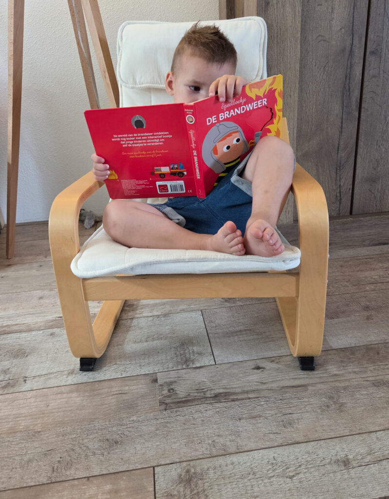 Jongetje uit het Kinderboekjes.nl kinderpanel zit in een kinderstoel en leest geconcentreerd het boekje De Brandweer.
