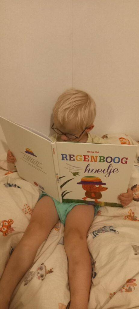 Jonge lezer uit het kinderpanel van Kinderboekjes.nl zit op bed en duikt geconcentreerd in het boek Regenboog hoedje van Hong Hai.